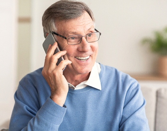 An older man on the phone and smiling after receiving his dental bridge