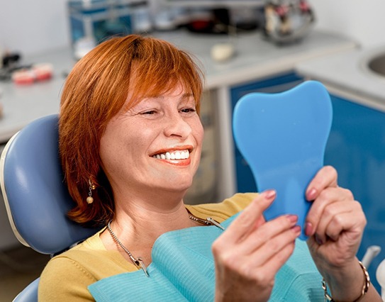 Woman smiling at reflection with dentures