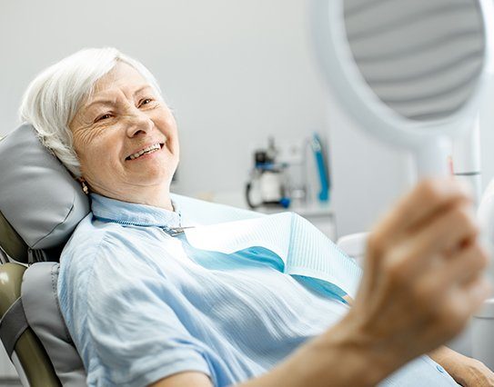 Older woman in dental office looking at smile with new dental bridge