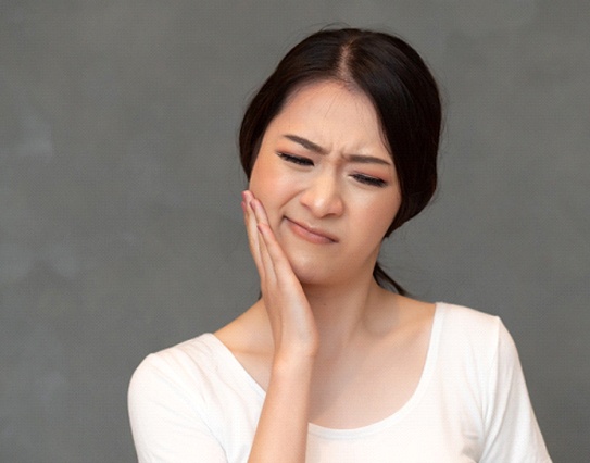 A young woman cringing and holding her jaw in discomfort