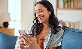 Woman smiling while looking at phone on couch