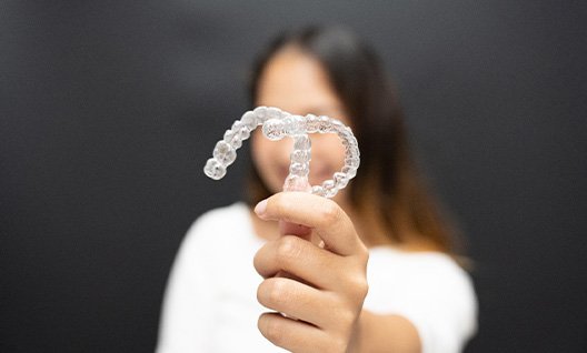 Woman holding a clear aligner and smiling