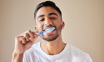 Man smiling while brushing his teeth