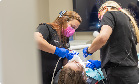 Two dentists treating patient in a chair