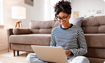 Woman in striped shirt sitting in front of couch working on laptop