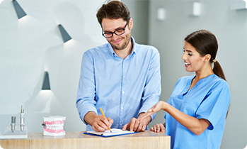 Man filling out form next to female dentist