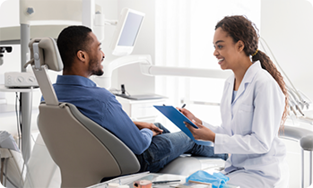 Female dentist with clipboard talking to dental patient