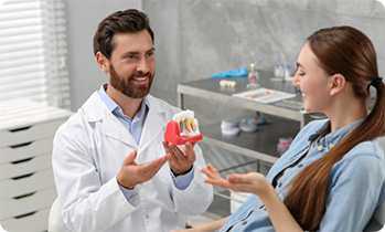 Male dentist showing female patient model of dental implant