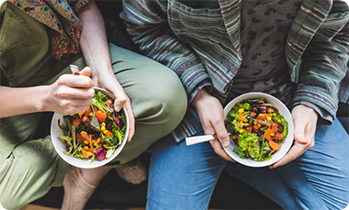 Close up of people holding bowls of salad in laps