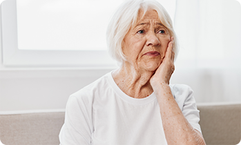 Senior woman on couch rubbing jaw in discomfort