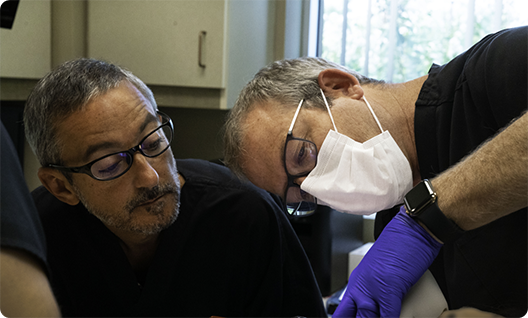 Dentist with mask working on patients mouth while another dentist watches