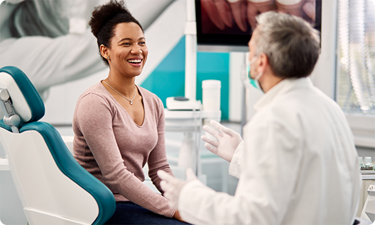 Woman sitting in dental chair smiling and talking to dentist