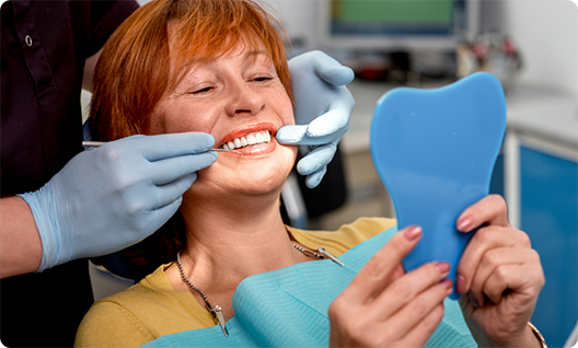 Red haired female dental patient checking smile in handheld mirror