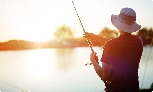 Man in floppy hat looking over lake while holding fishing rod