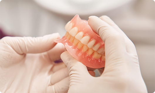 Gloved hands handling full dentures