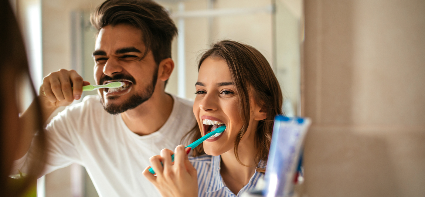 Man and woman brushing teeth in mirror