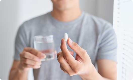 Man in grey shirt holding glass of water and a pill for sedation dentistry in Little Rock