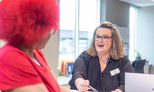 Front desk staff member talking to woman with glasses and red hair