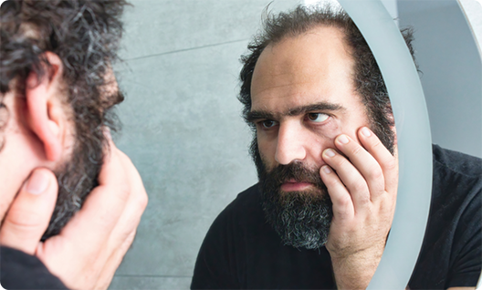 Concerned man rubbing jaw and looking in mirror