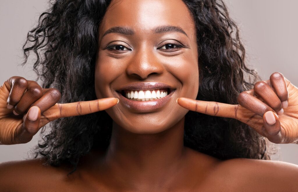 Woman with curly brown hair pointing to her perfect smile with both hands