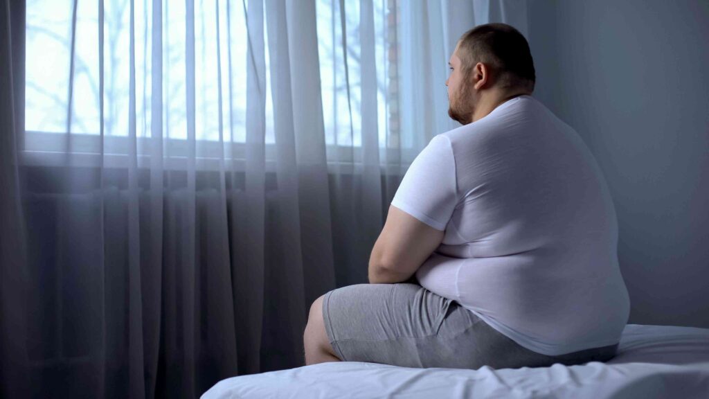 Overweight man sitting on a bed